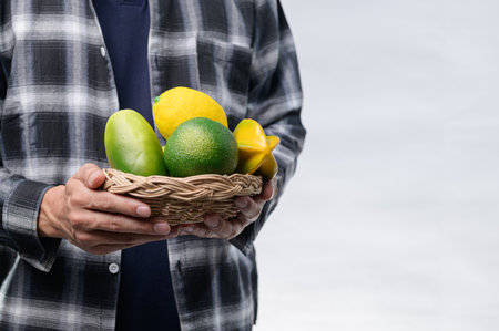A person in a plaid shirt holds a woven basket filled with colorful tropical fruits. The scene highlights the freshness and vibrant nature of healthy eating.の写真素材