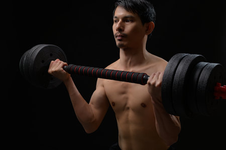 A determined man is lifting a heavy dumbbell, showcasing physical strength and fitness. The dark background highlights his focused expression and muscular form.の写真素材