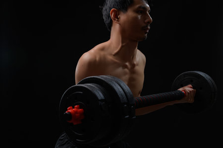 A dedicated individual performs a dumbbell lift in a dark setting, showcasing the commitment to strength training and personal health. Emphasizes focus and effort.の写真素材