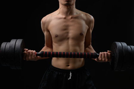 A focused male figure showcases strength and determination by lifting heavy dumbbells in a dark environment, emphasizing fitness and physical health.の写真素材