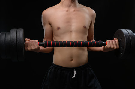 A muscular male figure lifts a dumbbell, showcasing strength and determination. The dark background highlights the focus on fitness and health training.の写真素材