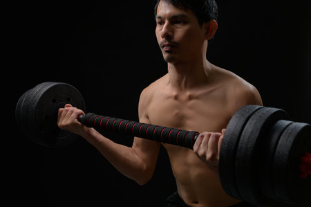 A young man engages in strength training with a heavy dumbbell, embodying determination and focus. The dark background emphasizes his commitment to fitness and health.の写真素材
