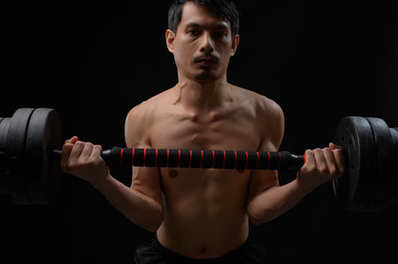 A focused young man demonstrates strength training by holding dumbbells in a well-lit fitness studio. The image captures his dedication to physical health and well-being.の写真素材