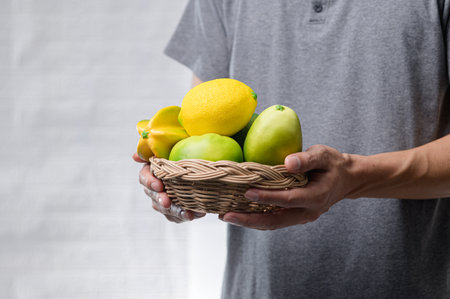 A woven basket filled with assorted fresh fruits showcases vibrant yellow lemons and green apples. This image emphasizes healthy eating and freshness.の写真素材