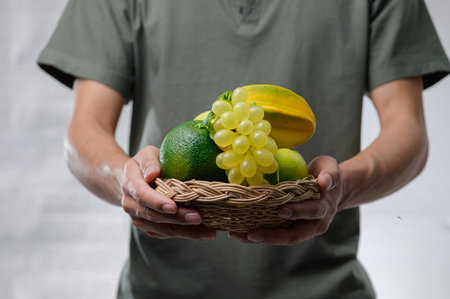 A person holding a woven basket filled with fresh organic fruits, including green avocados, yellow bananas, and grapes, showcasing healthy eating and lifestyle.の写真素材