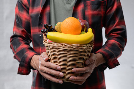 A man stands confidently holding a basket filled with a variety of fresh fruits, promoting a healthy lifestyle and vibrant nutrition options.の写真素材