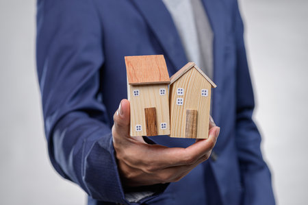 A person in a formal suit holds wooden model houses, representing real estate investment opportunities. This image captures the essence of architecture and property.の写真素材