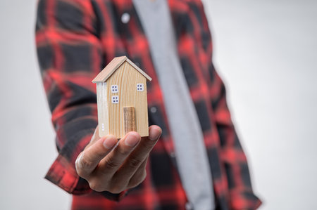 A person in a plaid shirt holds a handcrafted wooden model of a house, symbolizing dreams of homeownership and real estate investment.の写真素材