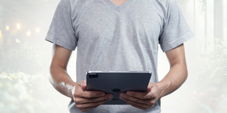 A person in a gray shirt holds a tablet with both hands. The background features soft focus, creating a calm atmosphere perfect for technology and lifestyle themes.の写真素材