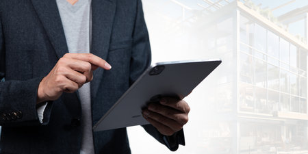 A stylish business professional engages with a tablet at a modern construction site, showcasing technology's role in contemporary architecture and project management.の写真素材