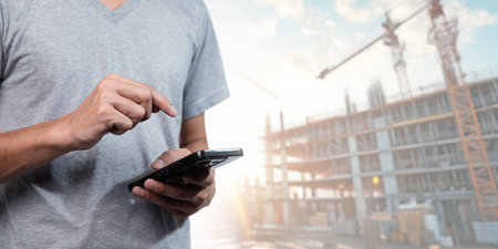 A construction worker interacts with a smartphone on-site, highlighting the fusion of technology and business in modern construction projects, capturing innovation in action.の写真素材
