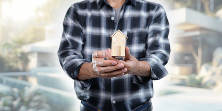 Explore the concept of buying and selling residential rental houses, illustrated through a model house held in hands. Ideal for real estate professionals and investors.の写真素材