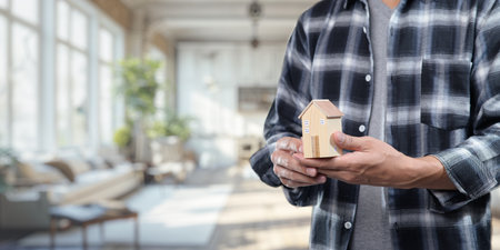 This image illustrates the concept of buying and selling residential rental houses, featuring a person holding a model home in a beautifully designed interior space.の写真素材