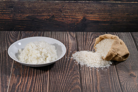 A close-up image of fresh white rice served in a bowl and spilling from a burlap bag on a rustic wooden table. Perfect for cooking and food-related projects.の写真素材