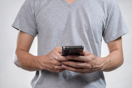 A person dressed in a gray shirt holds a smartphone in their hands against a neutral background, showcasing modern technology in everyday life.の写真素材