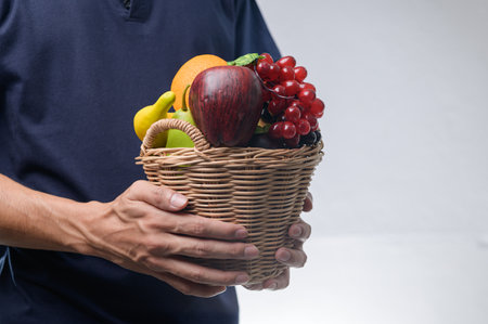 A person holds a vibrant basket filled with fresh fruits like apples, oranges, and grapes. This image conveys health, nutrition, and the joy of fresh produce.の写真素材