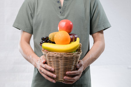 A person holds a woven basket filled with assorted fresh fruits, showcasing vibrant colors and textures, perfect for promoting healthy eating and lifestyle.の写真素材