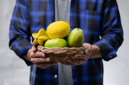 A person holds a woven basket filled with fresh fruits, showcasing vibrant colors. This composition captures the essence of healthy eating and nature's bounty.の写真素材