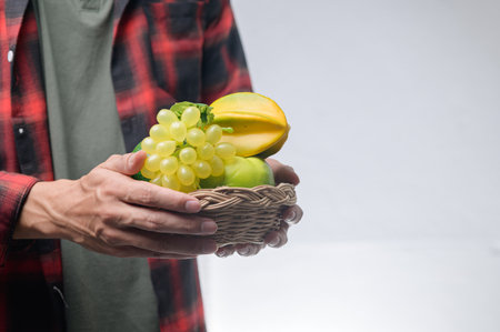 A person holds a basket filled with fresh fruits, featuring grapes, mango, and starfruit. The vibrant colors enhance the natural aesthetic of healthy eating.の写真素材