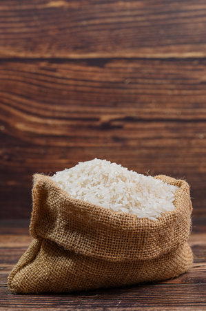 A close-up image of white rice in a burlap sack showcases the grain's texture against a rustic wooden backdrop, symbolizing natural and healthy cooking ingredients.の写真素材