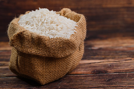 A burlap sack filled with fresh white rice sits on a rustic wooden surface, showcasing the natural beauty of this essential ingredient for many cuisines around the world.の写真素材