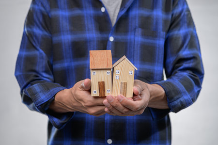 A person holds two charming wooden model houses, showcasing craftsmanship. The visual symbolizes home and security, ideal for real estate and lifestyle themes.の写真素材