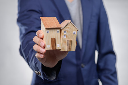 A businessperson in a suit holding two small model houses, symbolizing real estate investment and ownership. Ideal for marketing and financial presentations.の写真素材