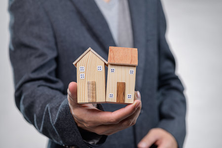 A businessman presents wooden model houses, symbolizing property investment and real estate opportunities. Ideal for presentations or financial concepts.の写真素材