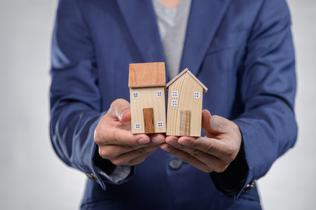 A business professional displays two small wooden model houses, symbolizing real estate investment and home ownership. The image conveys concepts of finance and design.の写真素材