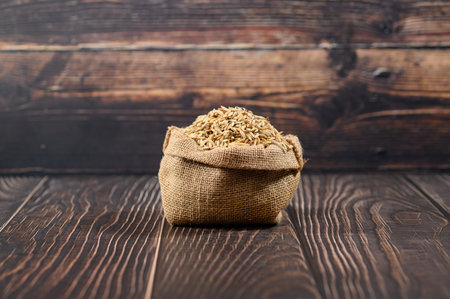 A rustic jute bag filled with brown rice resting on a wooden surface. This image symbolizes natural farming and healthy eating, perfect for culinary related content.の写真素材