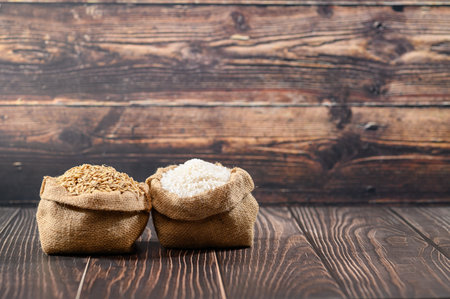 Two jute sacks filled with raw rice and oats sit on a rustic wooden table. The natural textures and colors highlight the organic origins of these grains.の写真素材