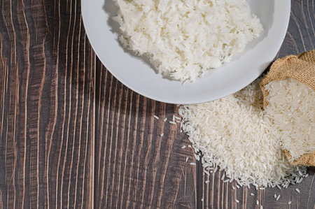 A bowl of freshly cooked rice placed on a rustic wooden table, with spilled grains nearby. This image captures the simplicity and natural beauty of staple food.の写真素材