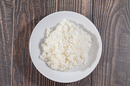 Enjoy a close-up view of fluffy white rice served on a plain plate, highlighting its delicate texture against a rustic wooden table. Perfect for culinary themes.の写真素材