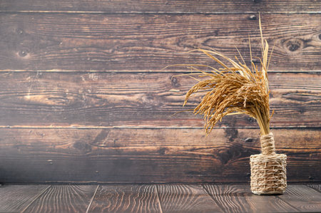 A unique arrangement of dried grass in a twine wrapped vase stands against a wooden background, creating a cozy and rustic atmosphere perfect for home decor.の写真素材