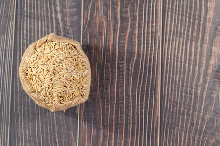 A burlap sack filled with raw oats rests on a rustic wooden table. This image captures the essence of wholesome grains, perfect for promoting healthy eating and sustainable agriculture.の写真素材