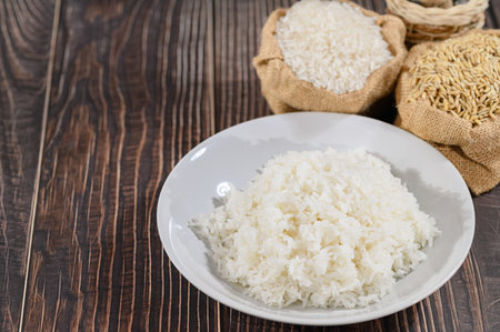 A beautifully presented plate of fresh cooked white rice sits in the foreground, with burlap bags of various rice grains beautifully arranged in the background, evoking a rustic feel.の写真素材