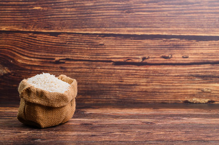A rustic scene featuring a burlap bag filled with raw rice placed on a wooden table. Ideal for food-related projects, showcasing natural ingredients in a warm setting.の写真素材