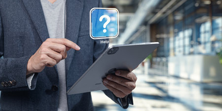 A person interacts with a tablet displaying a help icon in a sleek office setting. This image symbolizes digital assistance and user support in a modern workspace.の写真素材