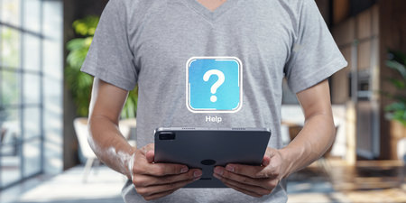 A person stands indoors, holding a tablet while wearing a T-shirt featuring a question mark icon. This scene conveys a theme of seeking help and assistance in a modern, casual environment.の写真素材