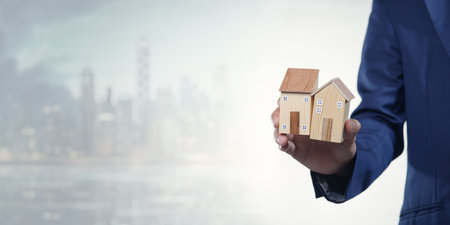 A professional person holds miniature model houses against an urban skyline, representing the concepts of selling, buying, and renting residential properties.の写真素材