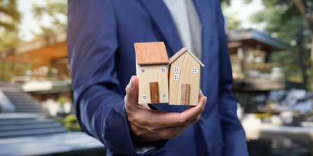 A professional holds miniature houses symbolizing real estate transactions. This image represents concepts of buying, selling, and renting residential properties.の写真素材
