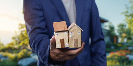 A professional individual holding model homes symbolizes the processes of selling and renting residential properties, highlighting the real estate market.の写真素材