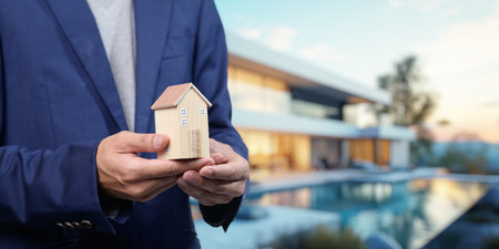 Professional individual holding a miniature house symbolizing the diverse aspects of selling, buying, and renting residential properties in todayの写真素材