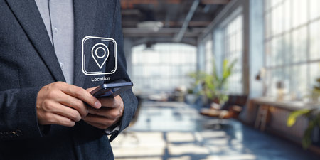A professional individual engages with a smartphone showcasing a location icon, set against a bright, modern office environment that emphasizes technology and connectivity.の写真素材