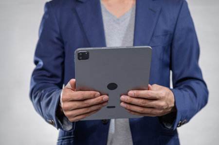 A confident businessman engages with a tablet in a modern office setting, showcasing technology's role in professional communication and productivity.の写真素材