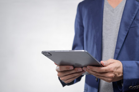 A person holds a tablet with a sleek design, dressed in a stylish blazer and casual tee, set against a minimalist white background, ideal for showcasing modern technology usage.の写真素材