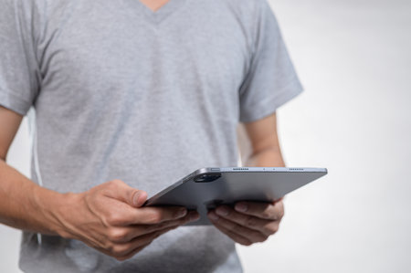 A person is holding a tablet computer while wearing a casual grey t-shirt. The image captures a modern lifestyle focused on technology and personal use of digital devices.の写真素材