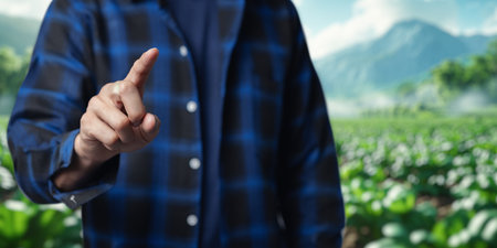 A person wearing a plaid shirt points a finger towards the viewer, set against a vibrant green agricultural field with a mountainous backdrop, symbolizing care and focus in farming practices.の写真素材