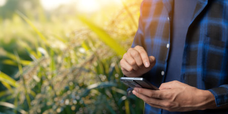 A person using a smartphone outdoors surrounded by lush greenery, highlighting the intersection of technology and business in a natural environment.の写真素材