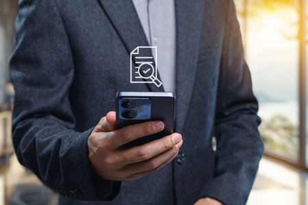 A businessman is checking a document on his smartphone in a modern office. The scene emphasizes...